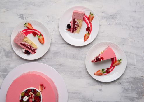 A top shot of berry mouse cake pieces served with a berry sauce on plates.