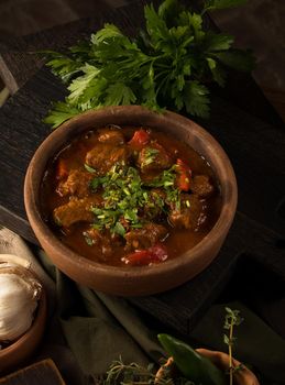 A close up shot of a meat stew and herbs in the background