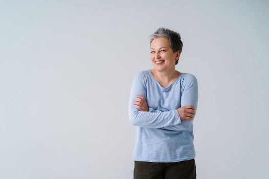 Feeling chills, smiling charming mature grey hair woman in 50s posing with hands folded and copy space on left isolated on white background. Place for product placement. Aged beauty concept.