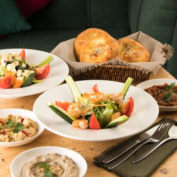 A dining table full of delicious salad on a white plate next to basket of bread