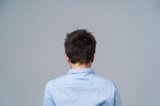 Grey short hair mature woman posing standing back to camera in blue shirt isolated on white background. Aged beauty.