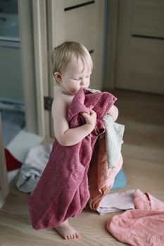 cute funny baby playing with stack of towels in the bathroom at home.