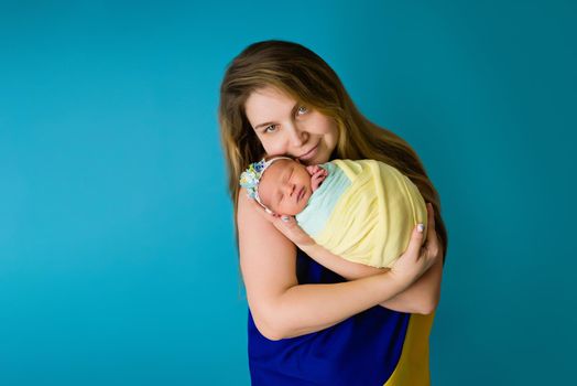 A Ukrainian mother in national yellow blue flag with an infant in the colors during the 2022 war. Close-up in the studio, insulated background. The most important heroes of women.