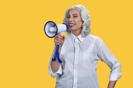 Portrait of cheerful mature businesswoman talking into megaphone on yellow background. Idea for marketing or sales.