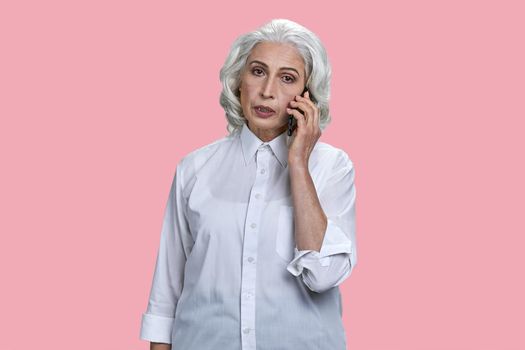 Portrait of elegant senior woman talking on mobile phone. Beautiful gray haired woman talking on cell phone on pink color background.