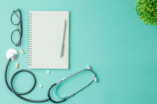 Open notebook with a pen and glasses on a green hospital background flat lay. top view. Nurse workplace concept. A stethoscope and pills on the doctor work desk.
