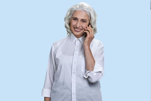 Happy senior business woman talking on mobile phone. Light blue background.