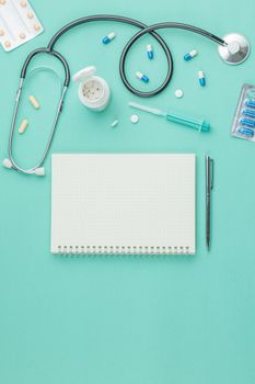 Medical equipment with stethoscope and spiral notebook in doctor office on green desk background top view. Nurse desktop concept.