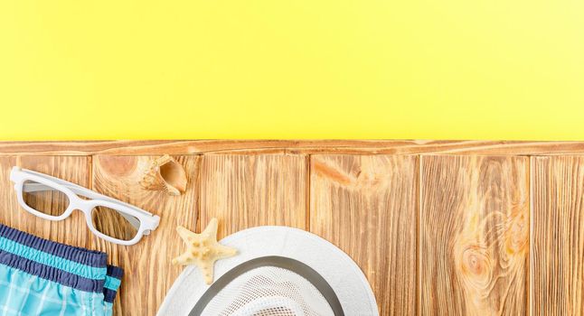 Beach hat with shorts and sunglasses on wooden background with a yellow copy space. Flat lay. Summer vacation concept. Starfish and seashell. Top view.