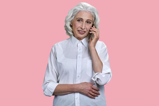 Beautiful senior business woman talking on cell phone on pink background. Mature woman using mobile phone on color background.