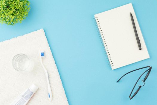 Toothbrush with toothpaste and glass of water on towel. Top view. Oral hygiene concept. Dentist table with notebook and pen on blue background.