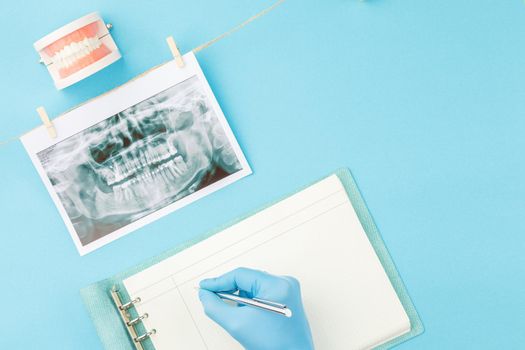Doctor makes notes in notebook while studying the x ray of the teeth. Top view. Dentist appointment concept.