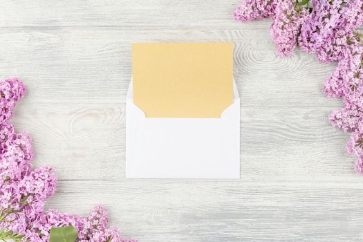 Open envelope with craft paper and lilac flowers on a white wooden background. Top view.