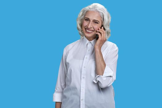 Portrait of cheerful mature business lady talking on mobile phone. Smiling senior woman talking on cell phone on blue background.