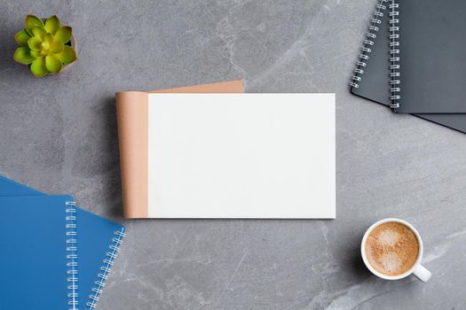 Open notebook with spiral notepads, a cup of coffee and a potted plant on a gray marble background. Top view.