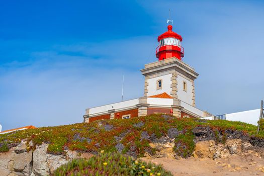 View of the Cabo da Roca Lighthouse. Sintra, Portugal. Portuguese Farol de Cabo da Roca is a cape which forms the westernmost point Eurasian land mass. Sunny summer day. Cloudy sky