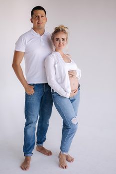 Happy future parents of man and pregnant woman puts hands on belly and waiting for beby movement in the belly. Studio photosession. Man dnd woman barefoot. Denim style.