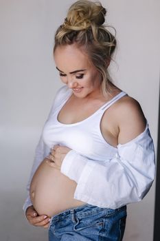 Close up portrait of pregnant woman in studio on white background. Beautiful future mother put her her hands on her belly. Stylish woman in white jaket