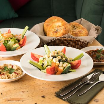 A dining table full of delicious salad on a white plate next to basket of bread