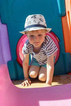 The little one is playing in a colorful, plastic playroom, he is training to crawl in a tube