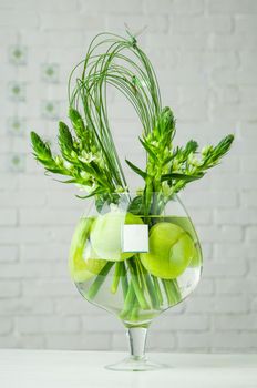 A vertical shot of Ornithogalum plant and apples in a large glass cup on a table