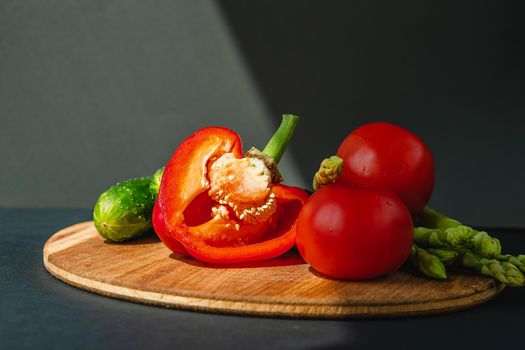 branches of fresh green asparagus, peppers, tomatoes and cucumbers on a wooden board, dark gray background, top view. Basic trend concept with copy space