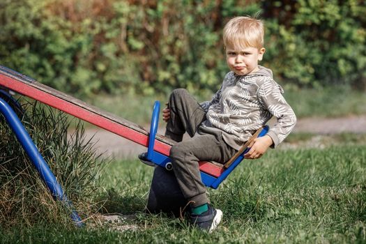 Boy is swinging on a balanced swinges in the evening in a playground at city park.