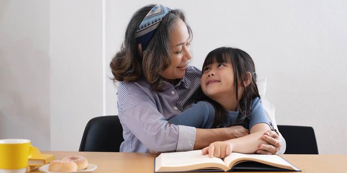 happy asian family grandmother reading to granddaughter child book at home