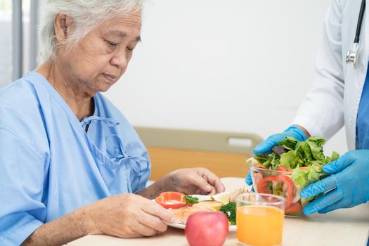 Asian senior or elderly old lady woman patient eating breakfast and vegetable healthy food with hope and happy while sitting and hungry on bed in hospital.