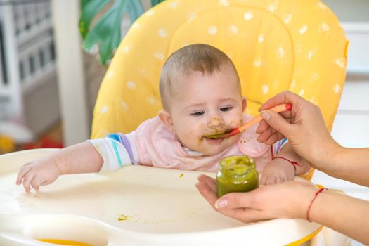 Little baby is eating broccoli vegetable puree. Selective focus. People.