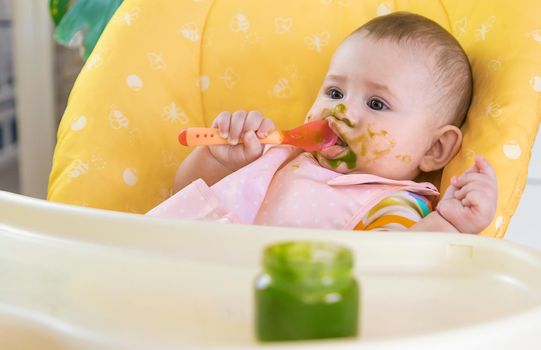 Little baby is eating broccoli vegetable puree. Selective focus. People.