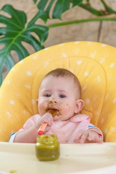 Little baby is eating broccoli vegetable puree. Selective focus. People.