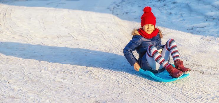 A child girl slides down a hill in the snow. Selective focus. People.