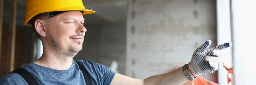 Portrait of foreman holding building plan and pointing outside window to look at business complex. Working on construction site. Renovation, build concept