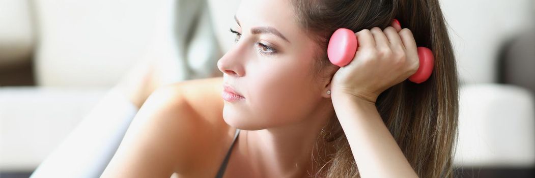 Portrait of young woman taking break between physical exercises laying on carpet. Pretty woman with pink dumbbells tool at home. Sport, weight loss concept