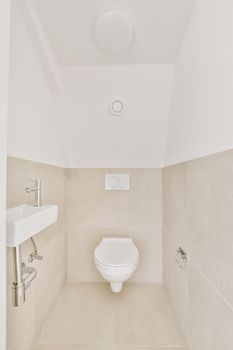 Wall hung toilet and small sink in corner in lavatory room with beige tile