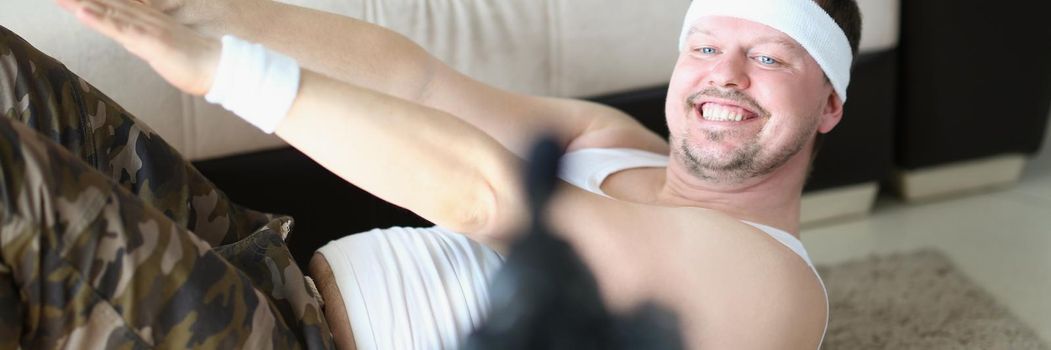 Portrait of man in sportswear perform exercise on carpet at home and film on camera. Active person start channel on social media. Internet, sport concept