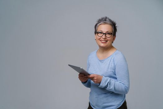 Businesswoman in eye glasses and digital tablet in hands working online smile looking at camera. Pretty woman in 50s in blue blouse isolated on white. Older people and technologies.