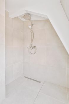 Shower faucets attached to tiled wall near glass partition and ornamental curtail in washroom at home