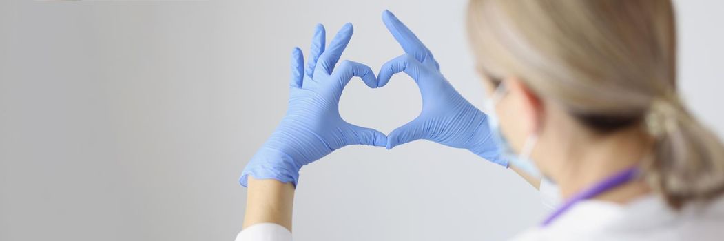 Close-up of medical worker form heart with hands wearing protective gloves. Nurse on day shift in hospital express support for patients. Medicine concept