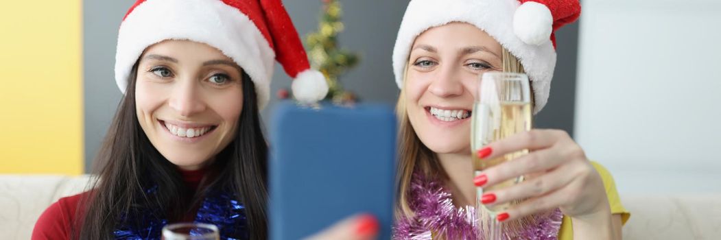 Portrait of cheerful sisters making selfie on smartphone holding champagne glasses. Merry atmosphere at home, family time. New year, christmas eve concept