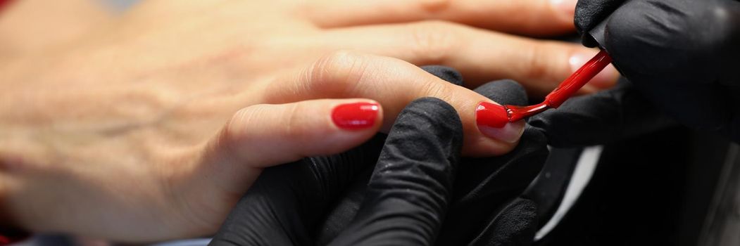 Close-up of professional salon worker cover clients nails with red colour polish. Refresh manicure at luxury beauty centre. Wellness, care, beauty concept