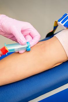 Nurse on pink gloves takes blood sample from vein from female patient in medical laboratory
