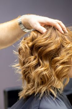 Side view of male hairdresser checks curly hairstyle of young caucasian woman in hair salon. Soft focus
