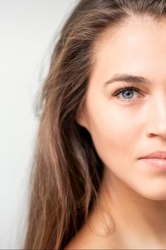 Half face portrait of young caucasian woman with natural make up and eyelash extensions looking at camera on white background