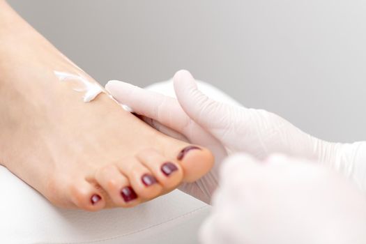 Pedicurist in white gloves massaging cream into woman leg in beauty salon