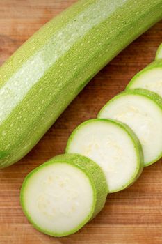 Slices of courgettes on wooden chopping board. Fresh green zucchini whole and cut into slices on cutting board