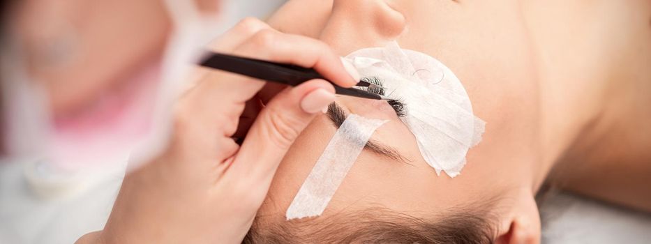 Young caucasian woman receiving eyelash extensions procedure in beauty salon