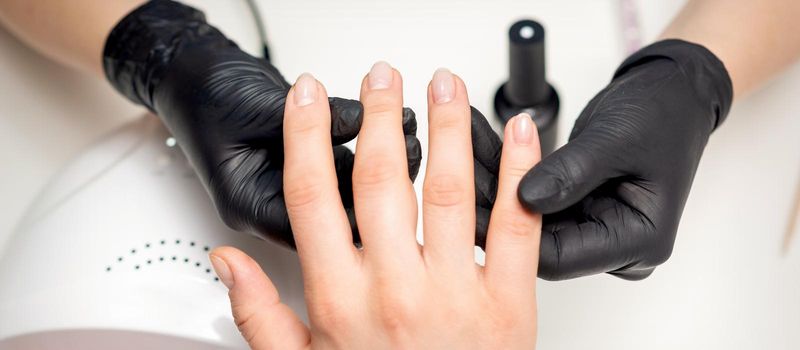 Top view close up of hands of manicurist in sterile black gloves holding client fingers in manicure salon