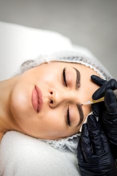 Top view of permanent makeup on eyebrows of young caucasian woman by special tattoo tool